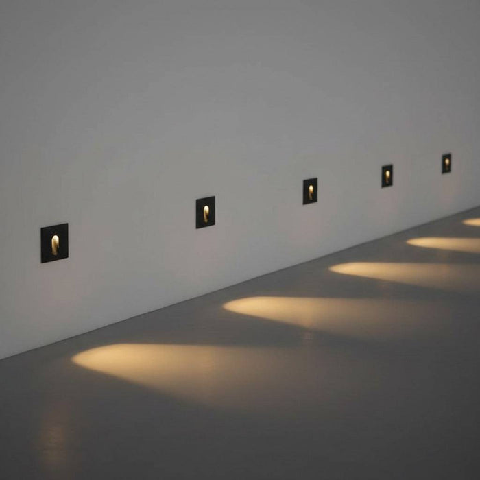 black outdoor step light fixture mounted in a row along a white wall outside
