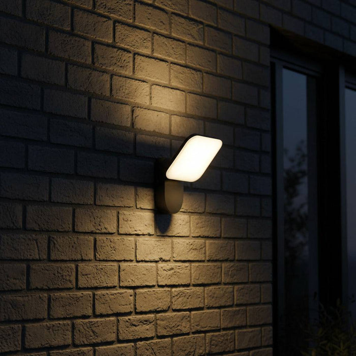 black external wall lamp mounted on a a grey brick wall outside a house