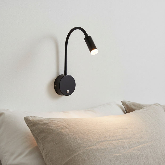 black dimmable reading light for bed mounted on the wall over a bed