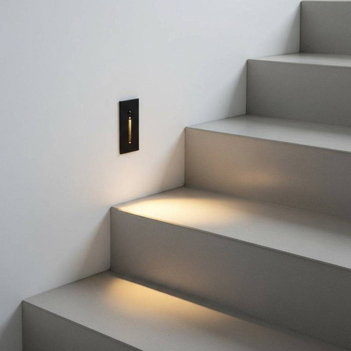 black sensor light for the stairs mounted in a white wall alongisde an indoor staircase