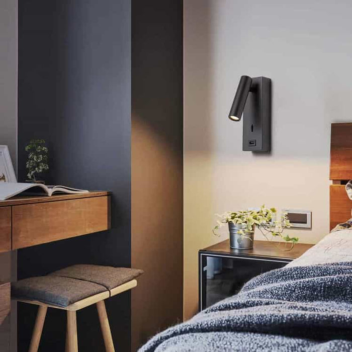 black wall mounted reading light with USB port mounted on a white wall next to a bed in a bedroom