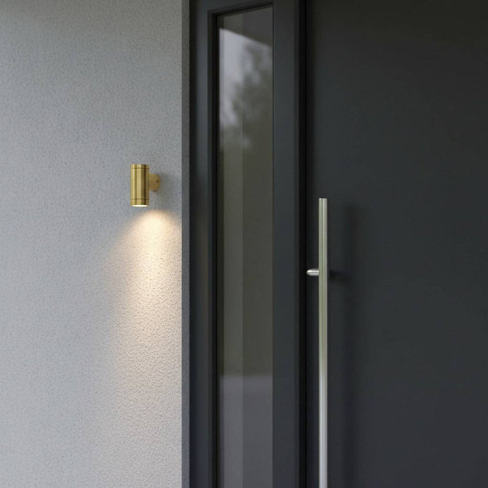 exterior brass wall light mounted on awhite textured wall outside the front door of a modern home
