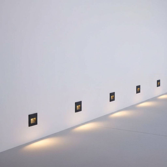 black stair step lighting mounted in a row on a white wall at low level