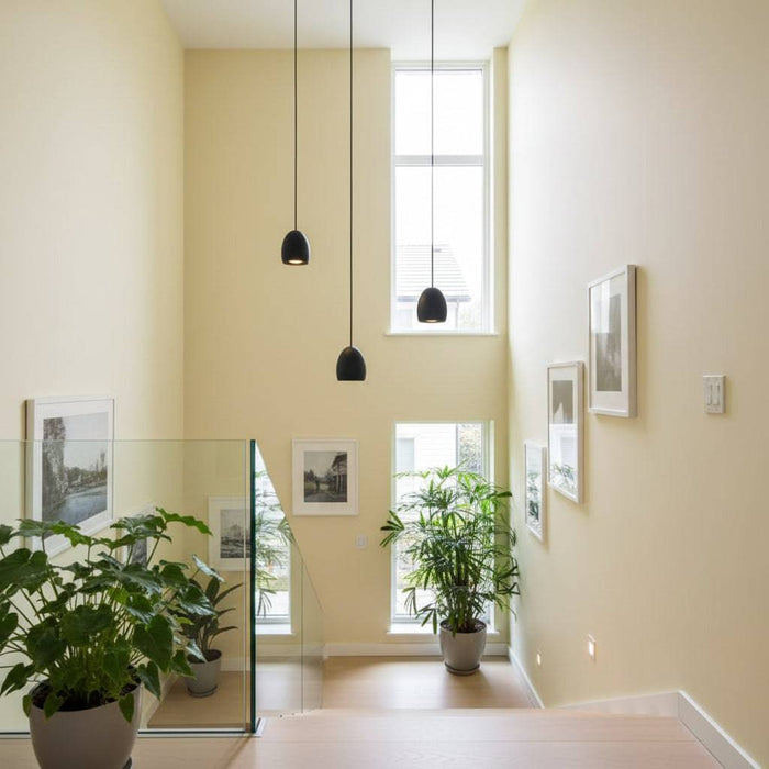 Black drop pendant lights above a stairwell with pale yellow walls and pictures and plants
