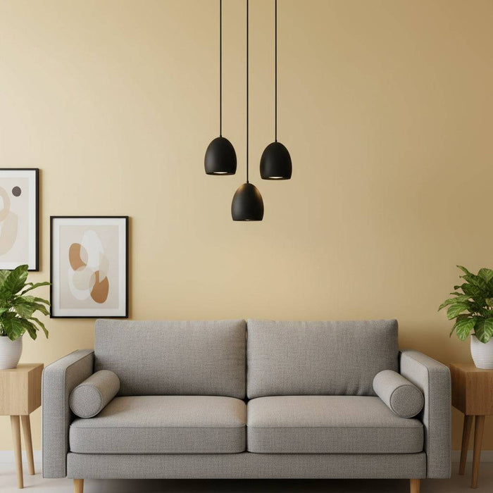 Three black drop pendant lights above a grey sofa with plants and pictures in a lounge