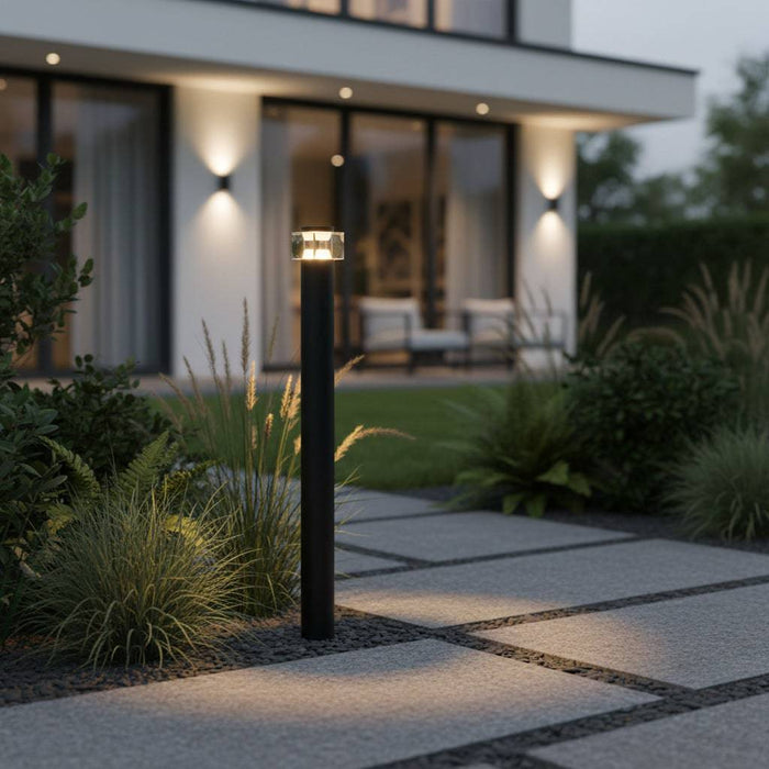 Black LED bollard path light illuminating an area leading to a modern home