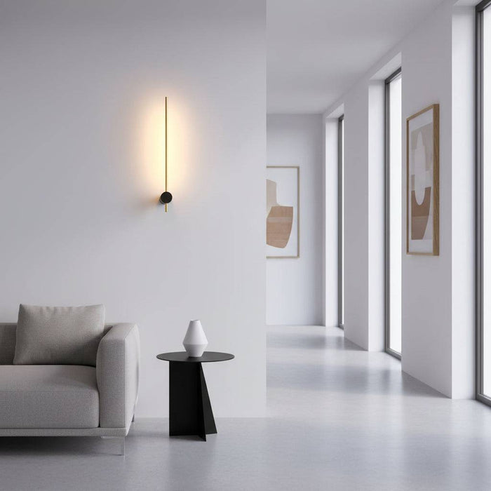 Black and gold interior LED wall sconce in a vertical  position on a plain wall in a modern house