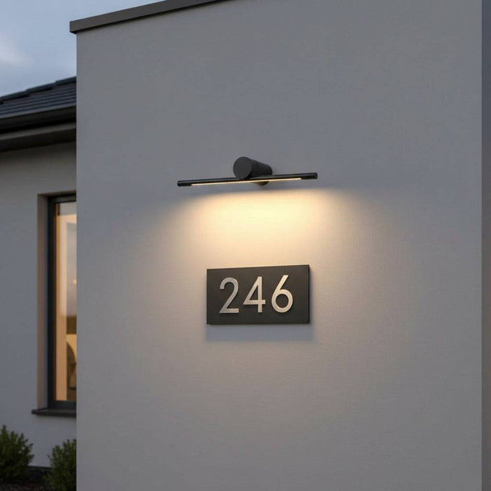 black sign wall light mounted over a house number on the wall of a modern house