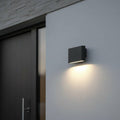 black outdoor LED wall downlight mounted on a white exterior wall next to the front door of a home