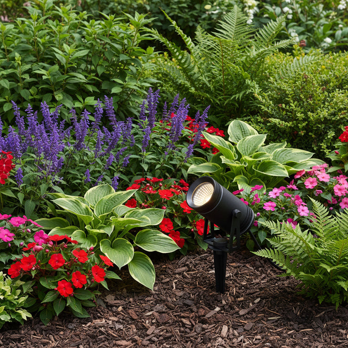 black LED stake light mounted in a planted garden border