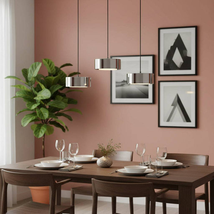 Hanging ceiling light fixture three lights above a dining room table with a plant and pictures against a pale red wall