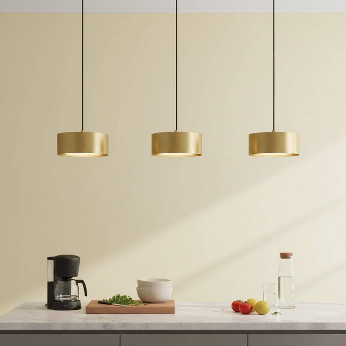 Gold pendant light above a kitchen worktop with fruit and coffee machine against a pale background