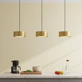Gold pendant light above a kitchen worktop with fruit and coffee machine against a pale background