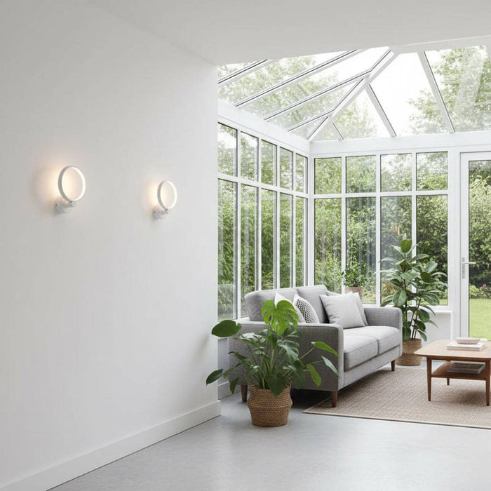 White indoor wall light fixture on a plain wall in a  conservatory  with furniture and pot plants