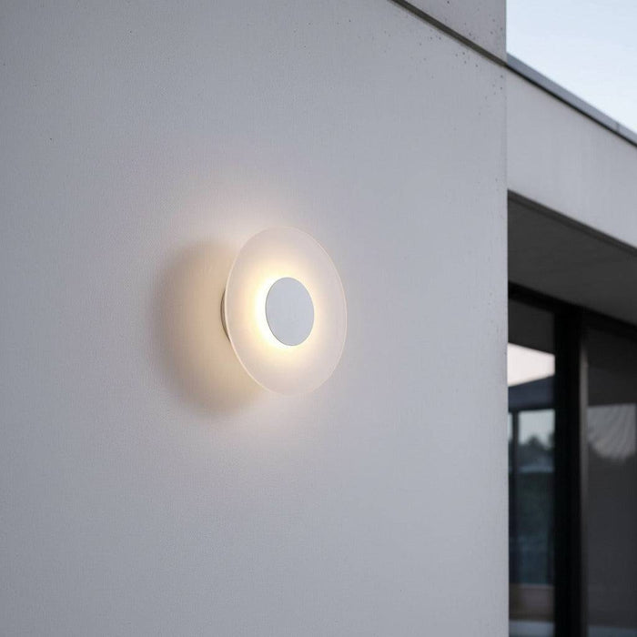 White round modern outdoor wall light mounted on a white wall of a modern home exterior