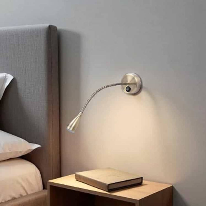 Antique finish flexible bedside reading light mounted on the wall next to a bed and over a bedside table
