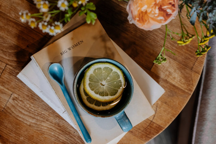 Teacup with lemon slice on a book, surrounded by flowers on a wooden surface