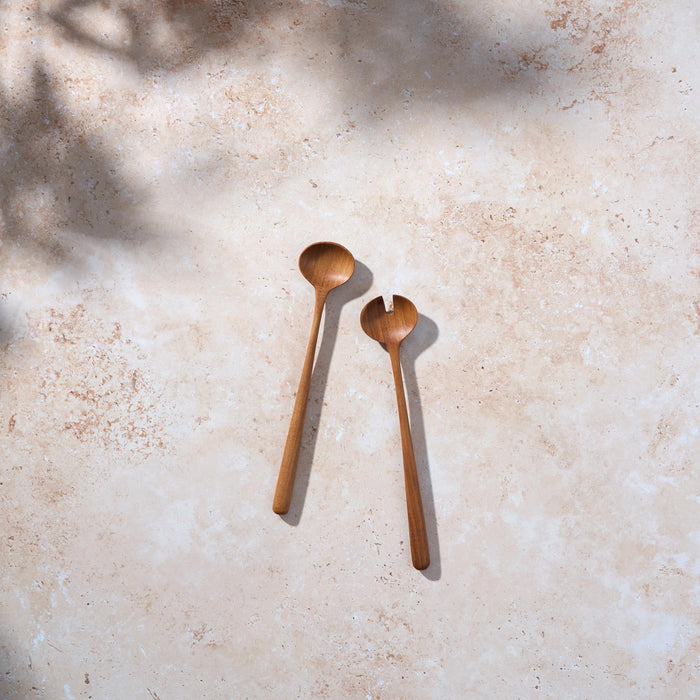 Bird’s-eye view of small retro teak wooden salad servers on a light stone background.