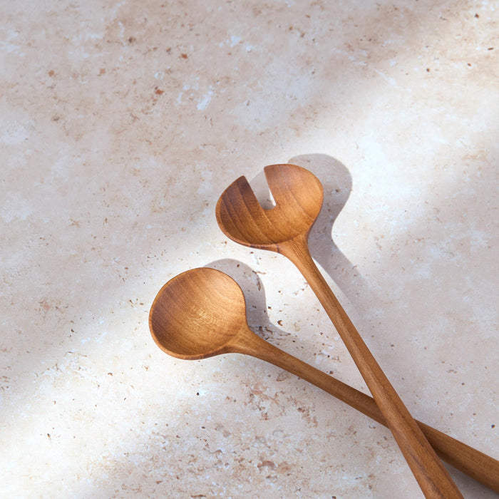 Angled shot of a retro teak wooden salad serving set by Palinopsia on a light stone background.