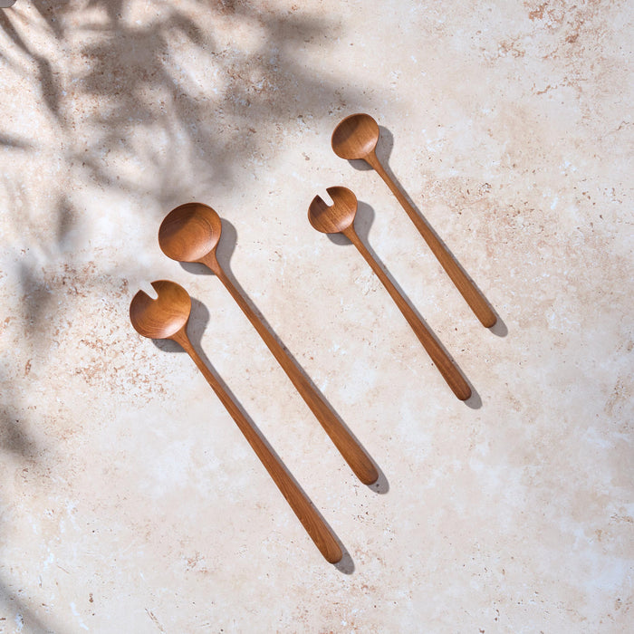 Bird’s-eye view of two sets, one large and one small, of large teak wooden salad servers on a light stone background.