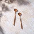 Bird’s-eye view of funky retro teak wooden salad servers on a light stone background.