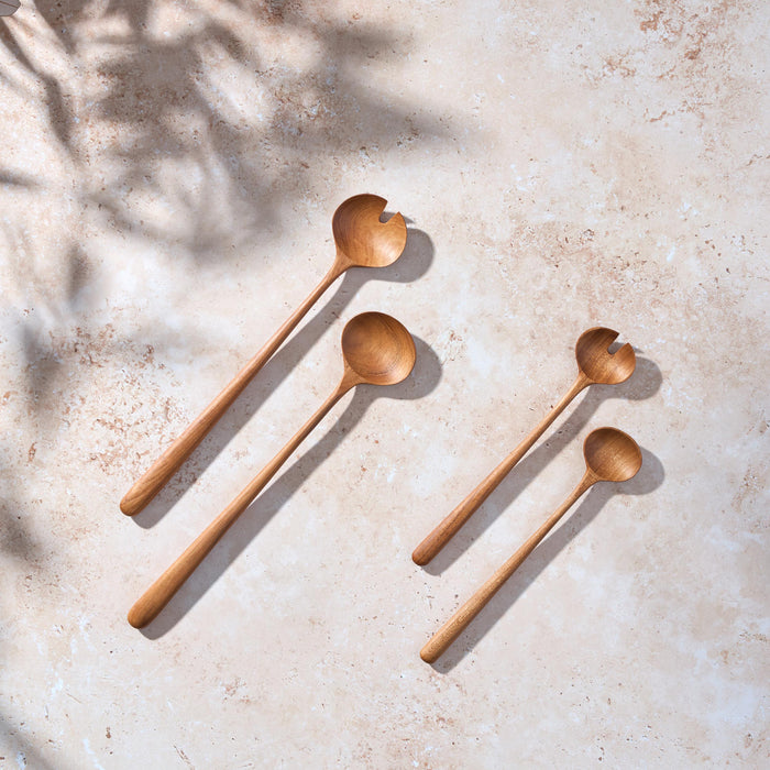 Bird’s-eye view of two set, one large and one small, of large teak wooden salad servers on a light stone background.