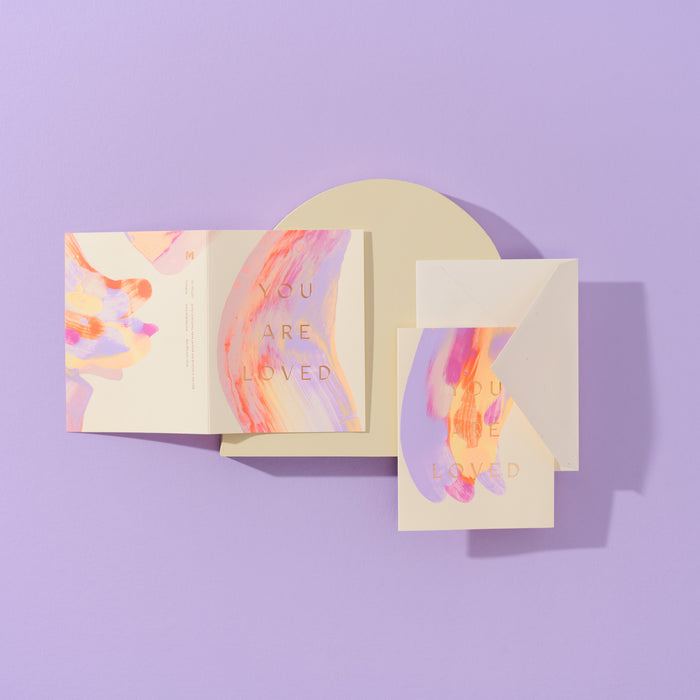 Two You Are Loved handmade purple artisanal greeting cards with purple, yellow and pink paint swirls and envelopes on a purple geometric background.