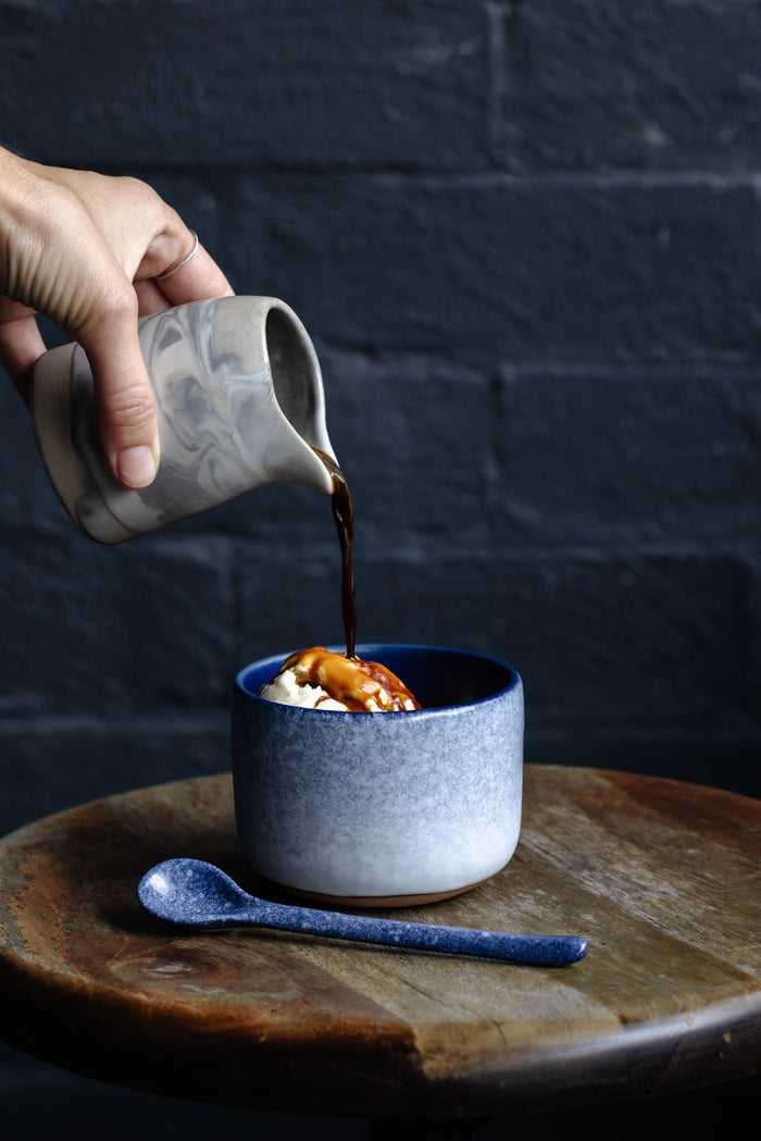Affogato, hand pouring coffee over ice cream in a Palinopsia winter themed tumbler cup on a stool with a dark navy background of Autumn Rooms cafe