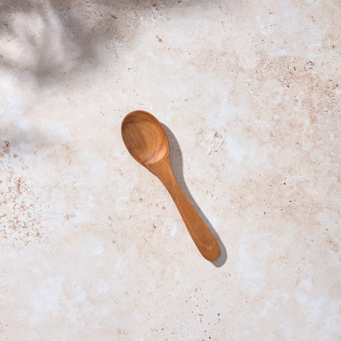 A Palinopsia teak wooden spoon on a light stone background.