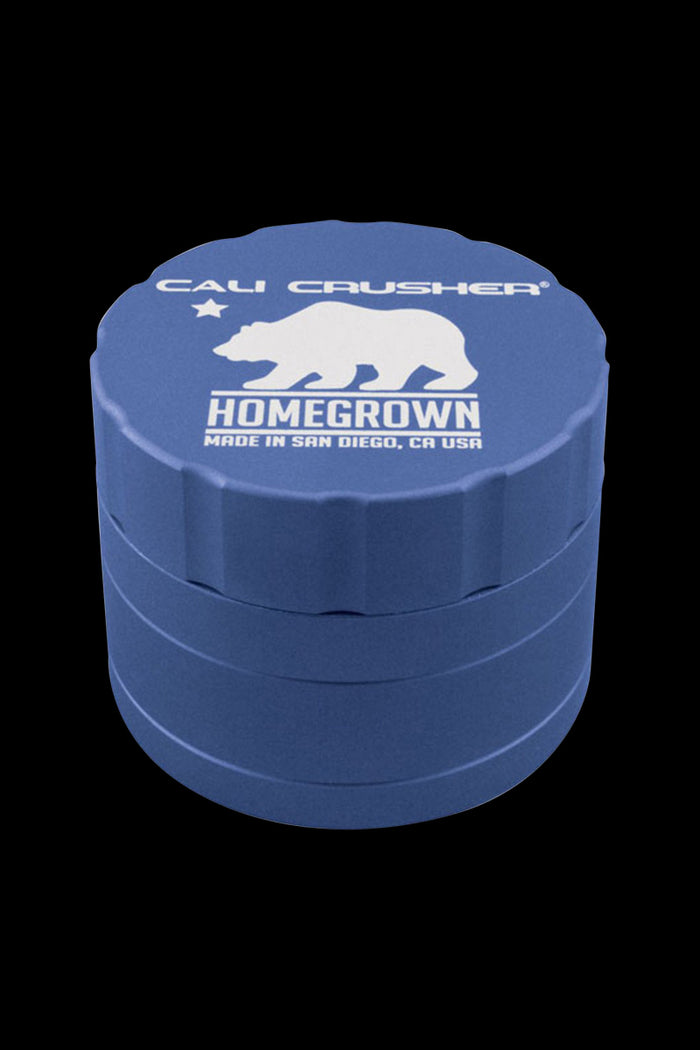 Angled top-down view of a blue Cali Crusher Homegrown 4-Part Grinder showing its stacked tiers and white bear logo on a black background.