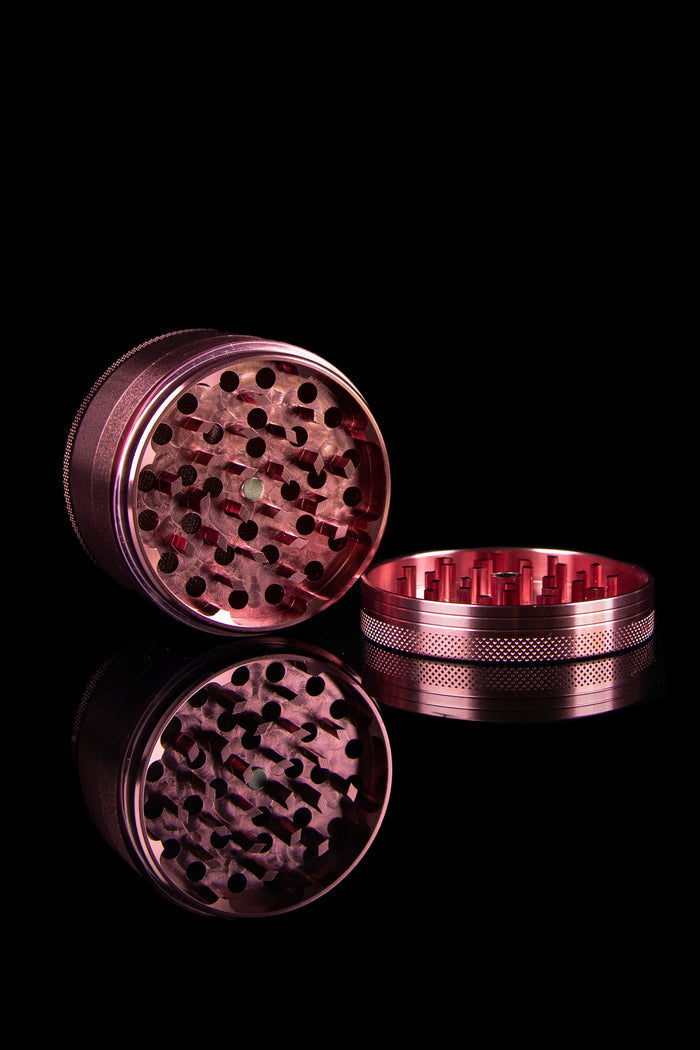Disassembled metallic cannabis grinder on a black background.