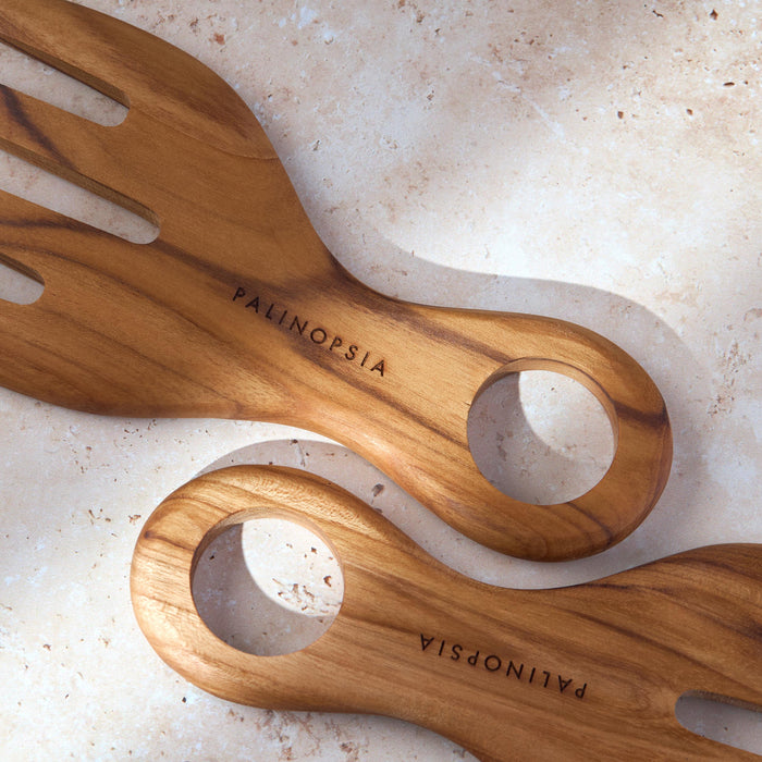 Close-up shot of a set of chunky teak wooden salad serving forks with the Palinopsia label on the handle on a light stone background.