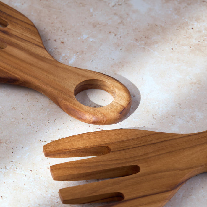 Close-up shot of a set of chunky teak wooden salad serving forks on a light stone background.