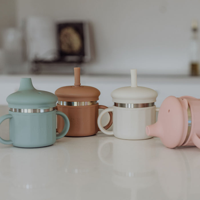 Four colorful children's sippy cups on a kitchen counter.