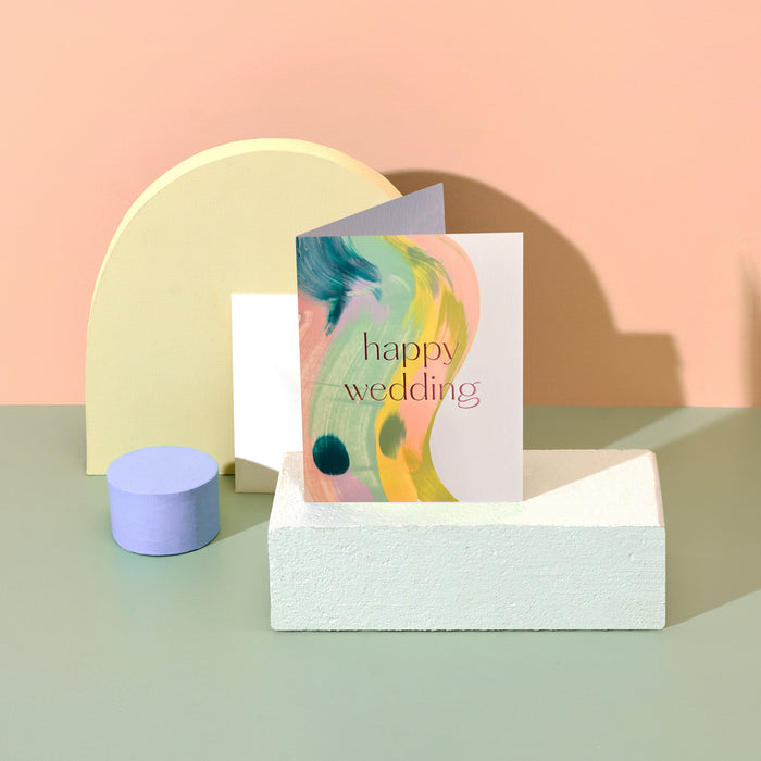 Happy Wedding handmade artisanal greeting card with bright colourful paint swirls and an envelope on a geometric background