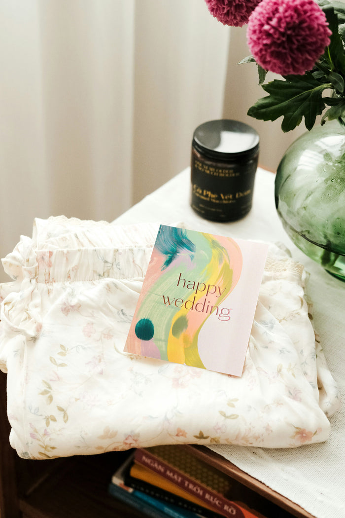 Happy Wedding handmade artisanal greeting card with bright colourful paint swirls on a table with wedding gifts in the background