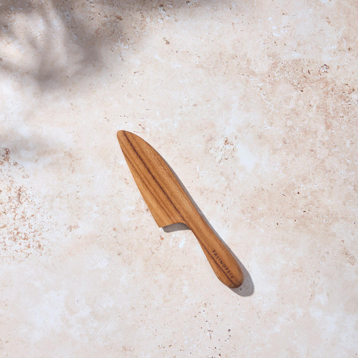 Bird’s-eye view of a Palinopsia wooden teak cheese knife on a light stone background.