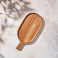 Bird’s-eye view of a Palinopsia teak wooden rectangular serving platter cheese board with a handle on a light stone background.