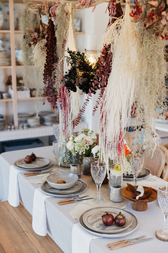Three piece ceramic stoneware dinner set in a marble abstract design set at a table with flowers hanging from above