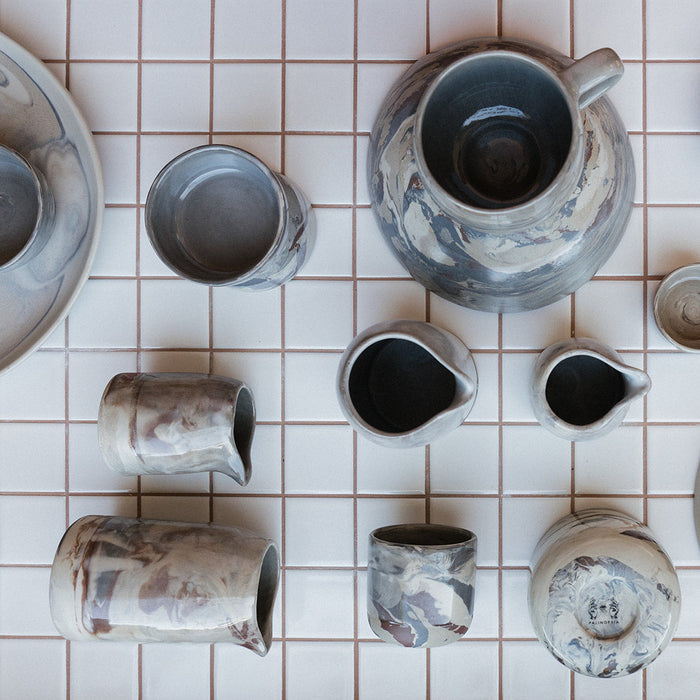 Palinopsia Marbled clay ceramic dinnerware mugs cups and hand pourers on tiled kitchen bench