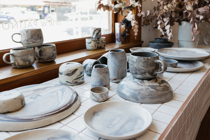 Tiled shelf in a shop with a ceramic handmade pitchers, bowls, plates and mugs in a neutral marbled clay design
