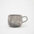 A handcrafted ceramic mug with a marbled pattern in shades of gray, with a handle on the right side, on a white background.