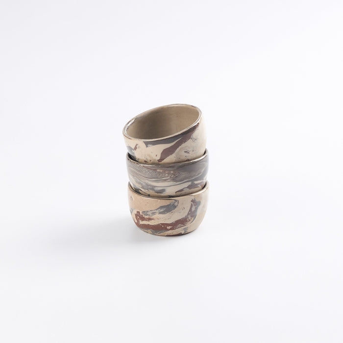 Stack of three ceramic small bowls with abstract marble patterns on a white background