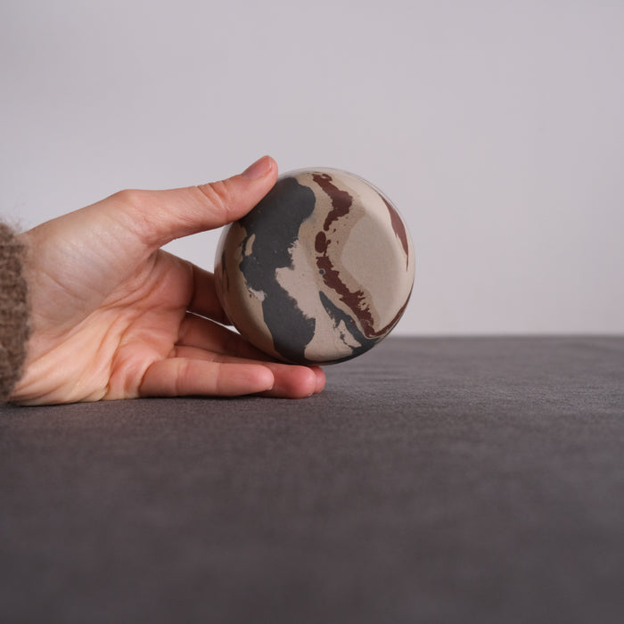 Hand holding a marbled clay small dish showing the reverse pattern against a dark background
