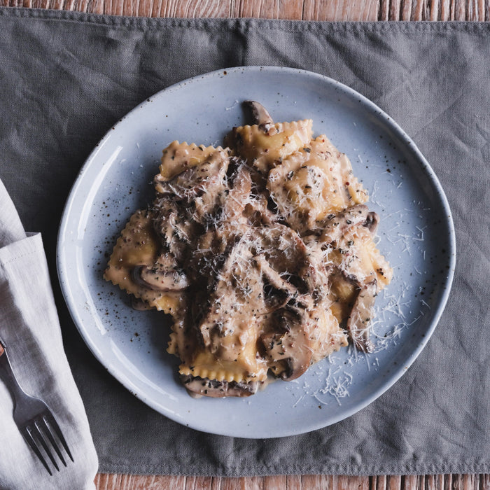 Roast duck ravioli alla boscaiola on a blue dinner plate and Palinopsia linen