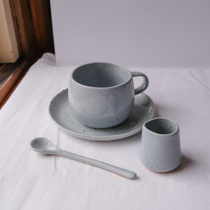 Handmade blue speckle coffee and tea mug by Palinopsia Ceramics with a teaspoon, and small ceramic milk pourer.