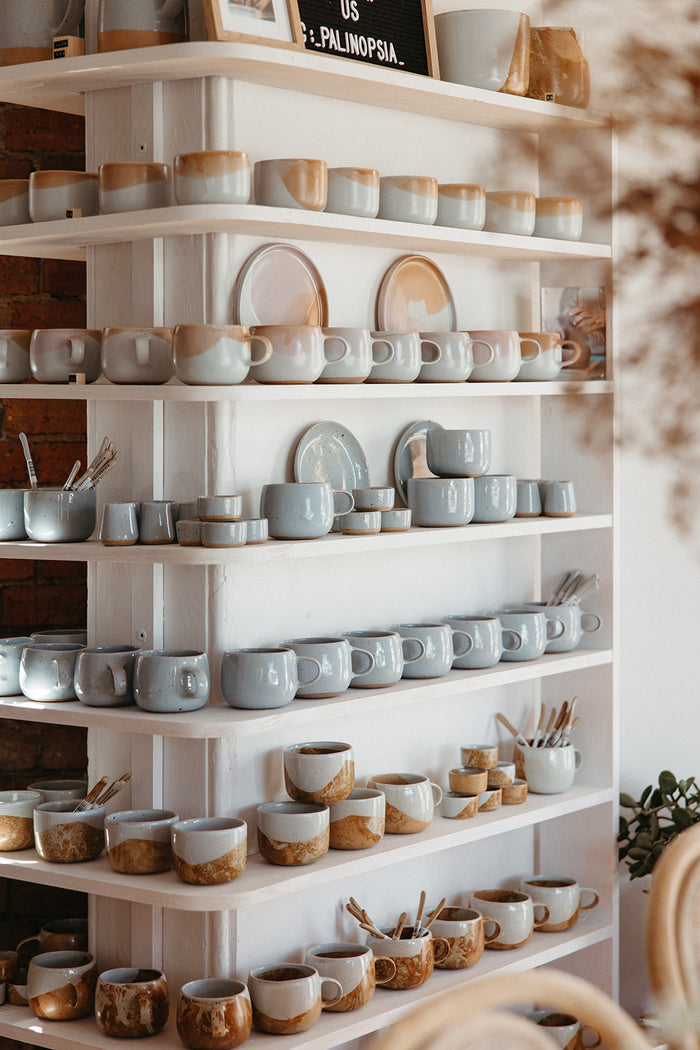 Curved shelf filled with stacked Palinopsia coffee and tea cups, mugs and teaspoons