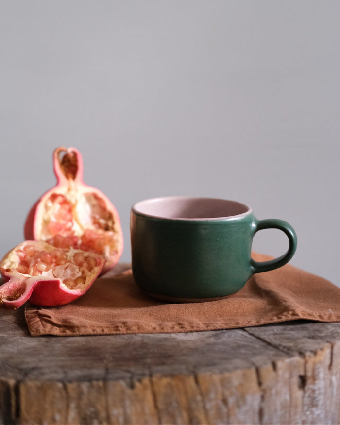 Dark green and pink stoneware mug on a brown napkin with pink pomegranate by Palinopsia