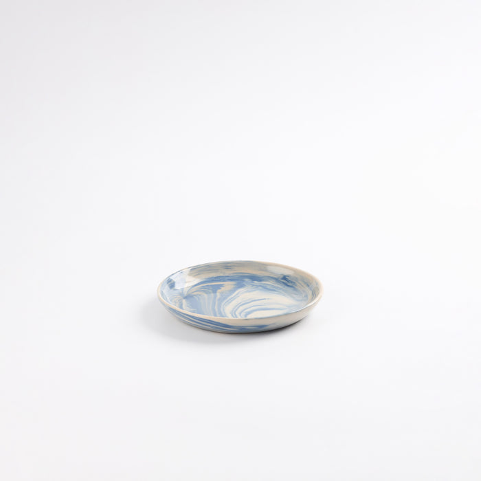 Small handmade ceramic plate with a marbled clay pattern in cobalt blue, beige and cream on a white background by Palinopsia