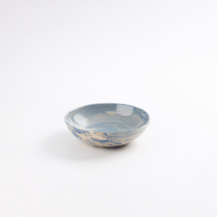 Handmade ceramic bowl with a marbled clay pattern in cobalt blue, beige and cream on a white background by Palinopsia
